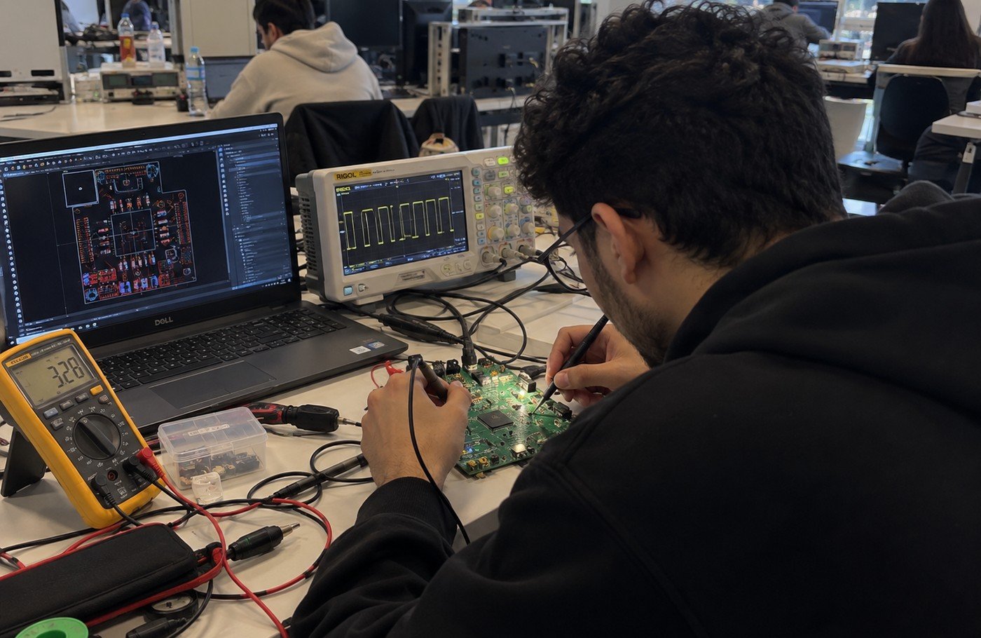 Un étudiant teste une carte PCB verte avec un multimètre et un oscilloscope